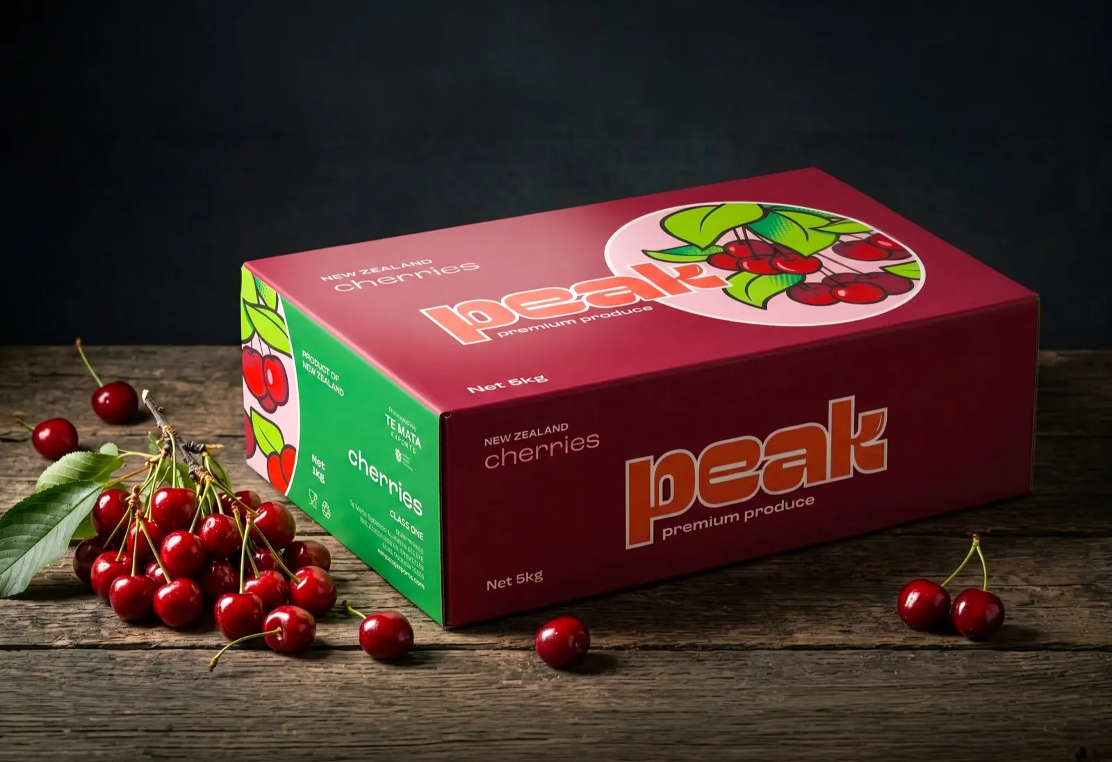 Peak branded New Zealand cherry carton on a wooden bench, with loose cherries beside it